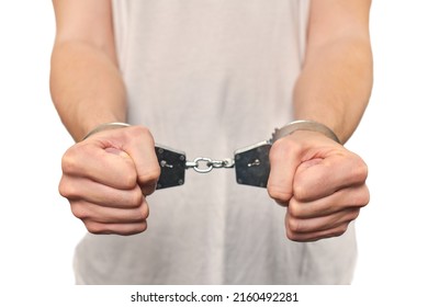 Hands of criminal in handcuffs, arrest of dangerous criminal isolated on white background, close up. Male fists locked in handcuffs, apprehension of offender in off-white T-shirt, violation of law