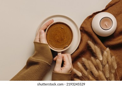 Hands with cup of coffee, linen cloth, dry lagurus grass and candle. Top view, flat lay, aesthetic minimal concept, brown tones - Shutterstock ID 2193245529