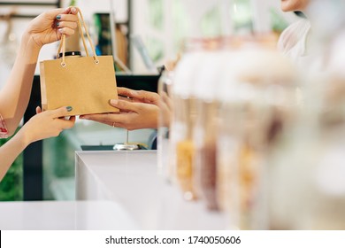 Hands Of Customer Taking Paper-bag With Her Order From Hands Of Shop Assistant