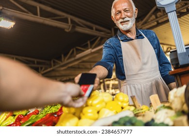 Hands of a customer and a vendor making transaction with a credit card and a pos terminal. A smiling seller charges for his vegetables at the stand. - Powered by Shutterstock