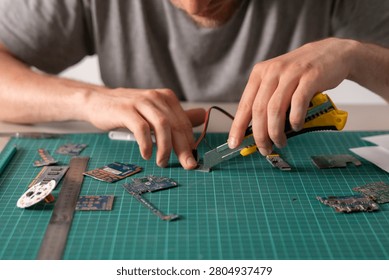 Hands cut circuit boards while working on electronics projects at a table in a well-lit area