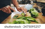 Hands, cutting board and salad in kitchen with green vegetables for healthy food or nutrition. Person with culinary skills for cooking lunch with lettuce, cucumber and organic ingredients at home