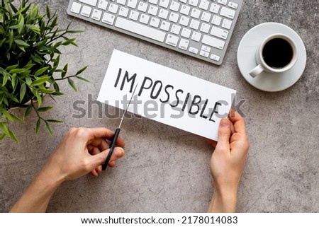 Hands cutting card with text Impossible into Possible. Motivation concept.