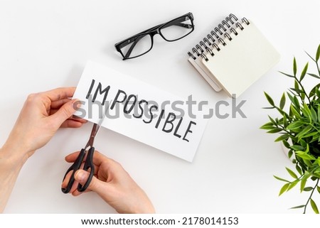 Hands cutting card with text Impossible into Possible. Motivation concept.