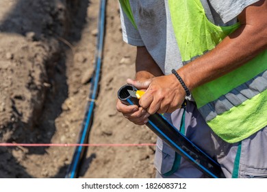 Hands Cutting Polypropylene Pipe In The Excavated Trench. 