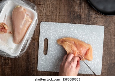 Woman’s hands cutting up raw chicken, gray cutting board, chef knife, black plate, wood table
 - Powered by Shutterstock