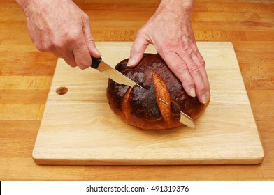 Hands cutting a rustic bread loaf on a wooden chopping board and kitchen worktop