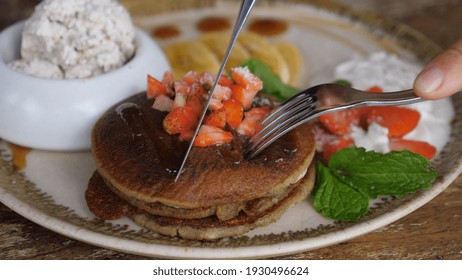 Hands cutting stack of pancakes with fork and knife. Healthy plant based breakfast 
