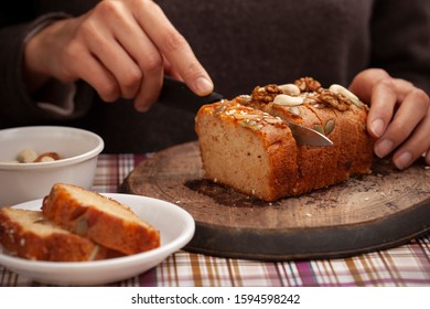 Hands Cutting Sweet Bread Cake Into Slice Through Knife On Wooden Board.