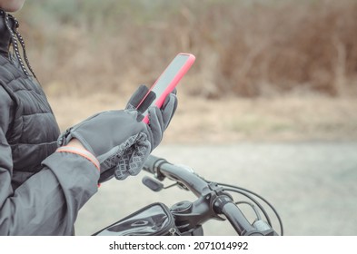 Hands of a cyclist in gloves hold a smartphone, close-up, mock-up. Traveler looking for directions using maps in smartphone