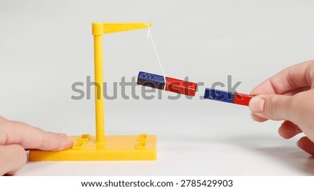 Hands demonstrate magnetic force using a suspended bar magnet and a second handheld magnet.
