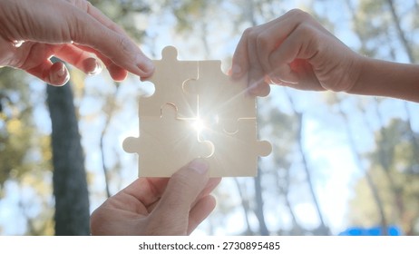 Hands of different generations join four wooden puzzle pieces outdoors, sunlight streaming through, symbolizing teamwork, unity, cooperation and shared progress toward a common goal