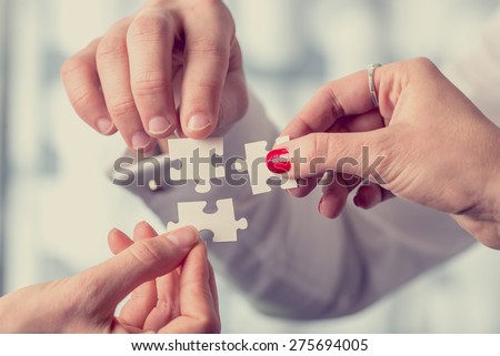 Hands of different people matching together three complementary puzzle pieces, concept of unity and problem solving, close-up with retro filter effect.