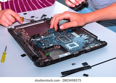 Hands disassembling a notebook with screwdriver; ports and connectors clearly visible in a technical close‑up.