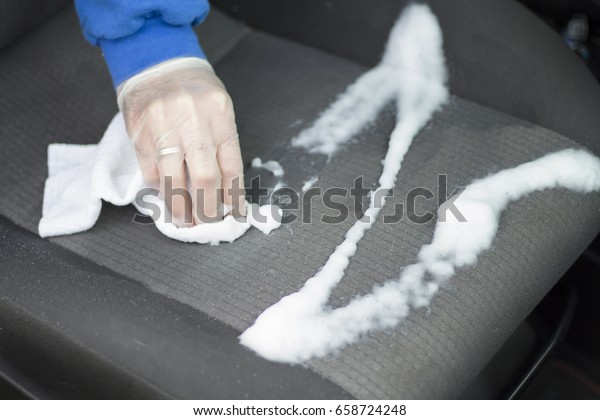 Hands in disposable gloves hold a white cloth with\
the seat of the car seat.