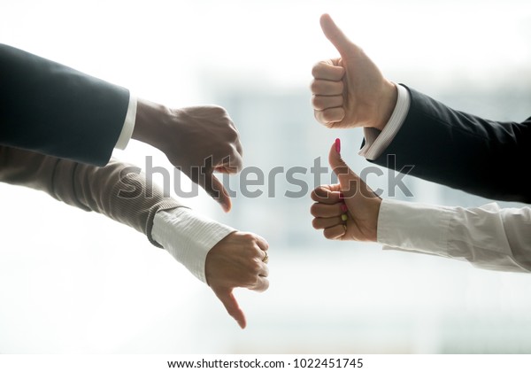 Hands of diverse business people showing thumbs\
up and down, like versus dislike gesture, positive negative\
feedback, yes and no opposition voting, confrontation disagreement\
at negotiations concept