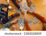 Hands of diverse group of senior friends playing with jigsaw puzzles in sunny dining room at home. Retirement, friendship, wellbeing, activities, togetherness and senior lifestyle, unaltered.