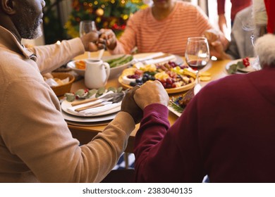 Hands of diverse group of senior friends saying grace at christmas dinner in sunny dining room. Retirement, friendship, christmas, celebration, meal, senior lifestyle, communication unaltered. - Powered by Shutterstock