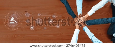 Hands of diverse individuals stack together symbolizing teamwork and collaboration in a legal context, integrated with digital icons of justice and technology on a wooden table. Trope