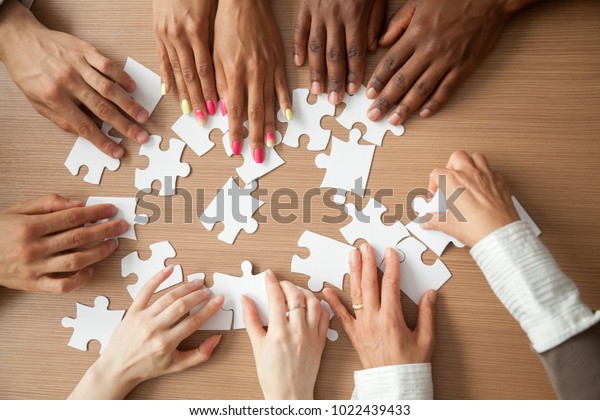 Hands of diverse people assembling jigsaw puzzle,\
african and caucasian team put pieces together searching for right\
match, help support in teamwork to find common solution concept,\
top close up view
