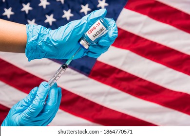 Hands Of Doctor Wear Gloves Holding Coronavirus (COVID-19) Vial Vaccine And Syringe On Flag United States Of America Background, USA Vaccination