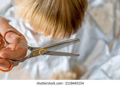 Hands Doing Toddler Haircut With Hairdresser Scissors With Thinning Layering Blade At Home. Baby Boy Hair Cut Diy