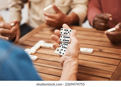 Hands, dominoes and friends in board games on wooden table for fun activity, social bonding or gathering. Hand of domino player holding rectangle number blocks playing with group for entertainment