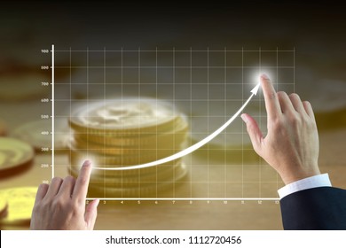 Businessman’s Hands Drawing A Line Graph Showing Of Business Growth And Success With Golden Tone Of Money Stack On Background.