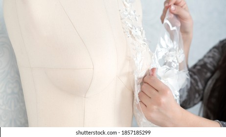 Hands of dressmaker or tailor is arranging lace fabric on a mannequin. Working sewing process of a fashion designer at her studio.
