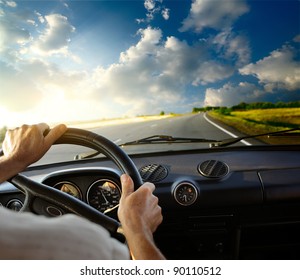 Hands of a driver on steering wheel of a car and empty asphalt road