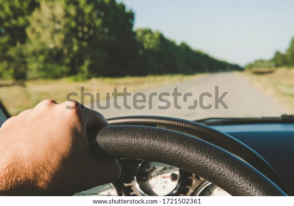 Hands of a driver on steering wheel of a car and\
empty asphalt road. Riding behind the wheel of a car in summer.\
first-person view. drive on the highway outside the city. to stay\
behind the wheel.