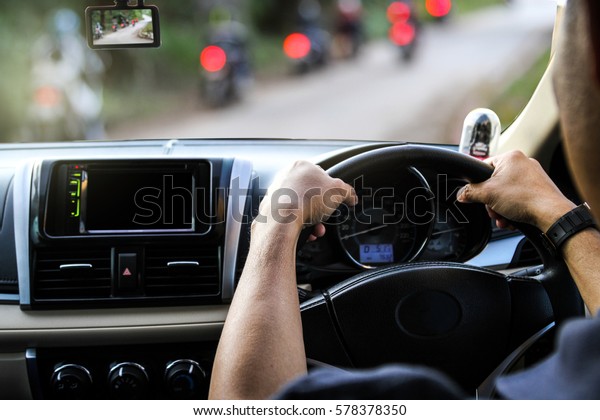Hands of a\
driver on steering wheel of a car on\
road