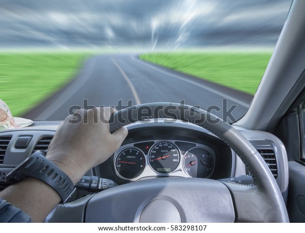 Hands of a driver on steering wheel of a car and\
empty asphalt road,very\
fast