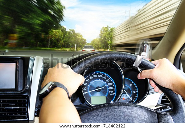 Hands of a driver on steering wheel of a car and
empty asphalt road.