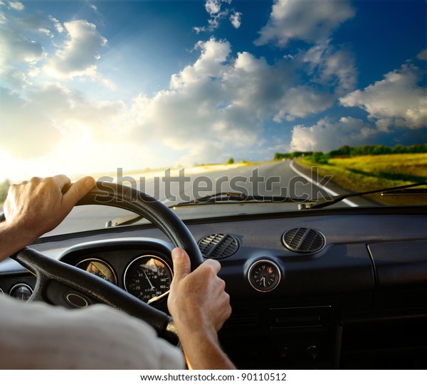 Hands of a driver on steering wheel of a car and\
empty asphalt road