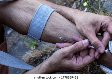 Hands of a drug addict with a syringe full of narcotic, heroin or cocaine to the leg veins. Drugs addiction, obsession, abstinence crisis and withdrawal symptoms concept. Close up.