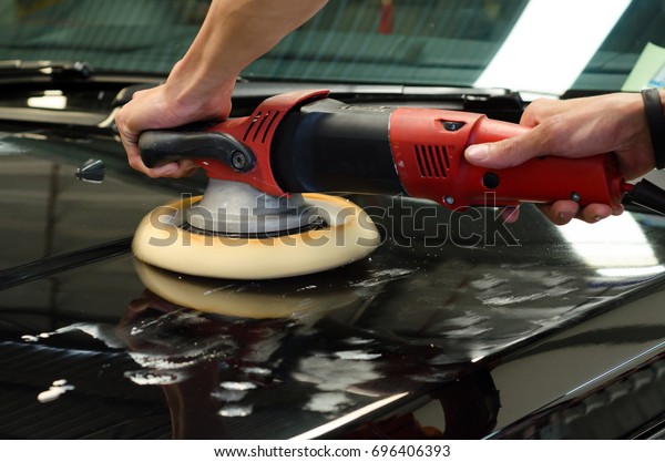 Hands with dual action polisher. polishing on car\
surface. hand and foam pad in blur motion from vibration of\
polisher machine