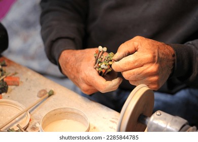 Hands of elderly craftsman man working in a workshop polishing opal stones and minerals to form precious jewelry - Powered by Shutterstock