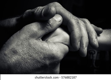Hands of an elderly man holding the hand of a younger man. Lots of texture and character in the old man hands. black and white