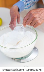 Hands Of An Elderly Man Using A Scales On A Table To Weigh Flour In A Kitchen