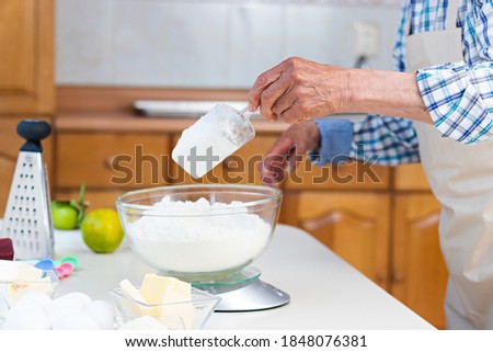 Hands of an elderly man using a scales on a table to weigh flour in a kitchen