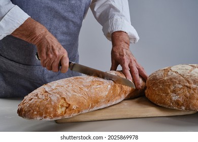 The hands of an elderly person hold and cut bread with a knife. Freshly baked bread in senior wrinkled hands. Selective focus - Powered by Shutterstock