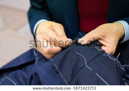 The hands of an elderly tailor basting and sewing the men's jacket. Sartorial clothes are made by hand