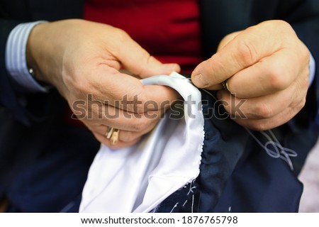 The hands of an elderly tailor basting and sewing the men's jacket. Sartorial clothes are made by hand