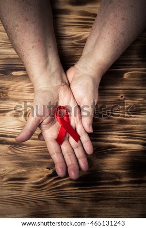 Hands of elderly woman and an international symbol of the fight against breast cancer on light burned wooden background. Toned.