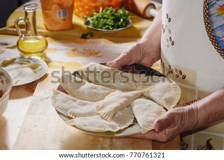 The hands of an elderly woman prepare a pie of thin fresh dough with stuffed minced meat and spicy seasonings	