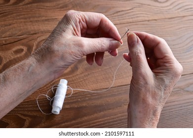  Hands Of An Elderly Woman Thread A Needle. Tailor's Hands Close-up. Handmade Work. Needlework And Sewing