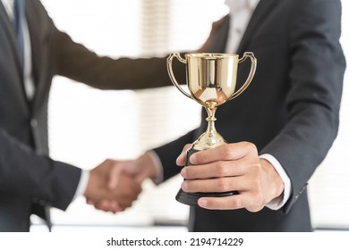 The hands of an employee receiving a golden cup reward from the company manager represent his performance in his career job reward. - Shutterstock ID 2194714229