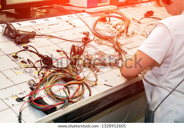 Hands of employees who check the quality of the\
wiring for cars at a modern plant on a special stand at the\
production shop