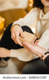 Hands exchanging small gift box in warm light. Close-up of two people exchanging a small cardboard gift box in cozy golden light, symbolizing kindness, giving, and celebration.